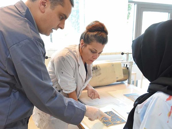 Workshop participants examining a print beside a press at Zayed University in Abu Dhabi