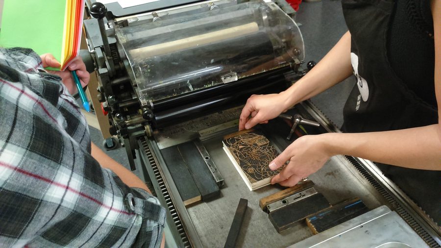 Hands positioning a laser-engraved block in a printing press during a workshop